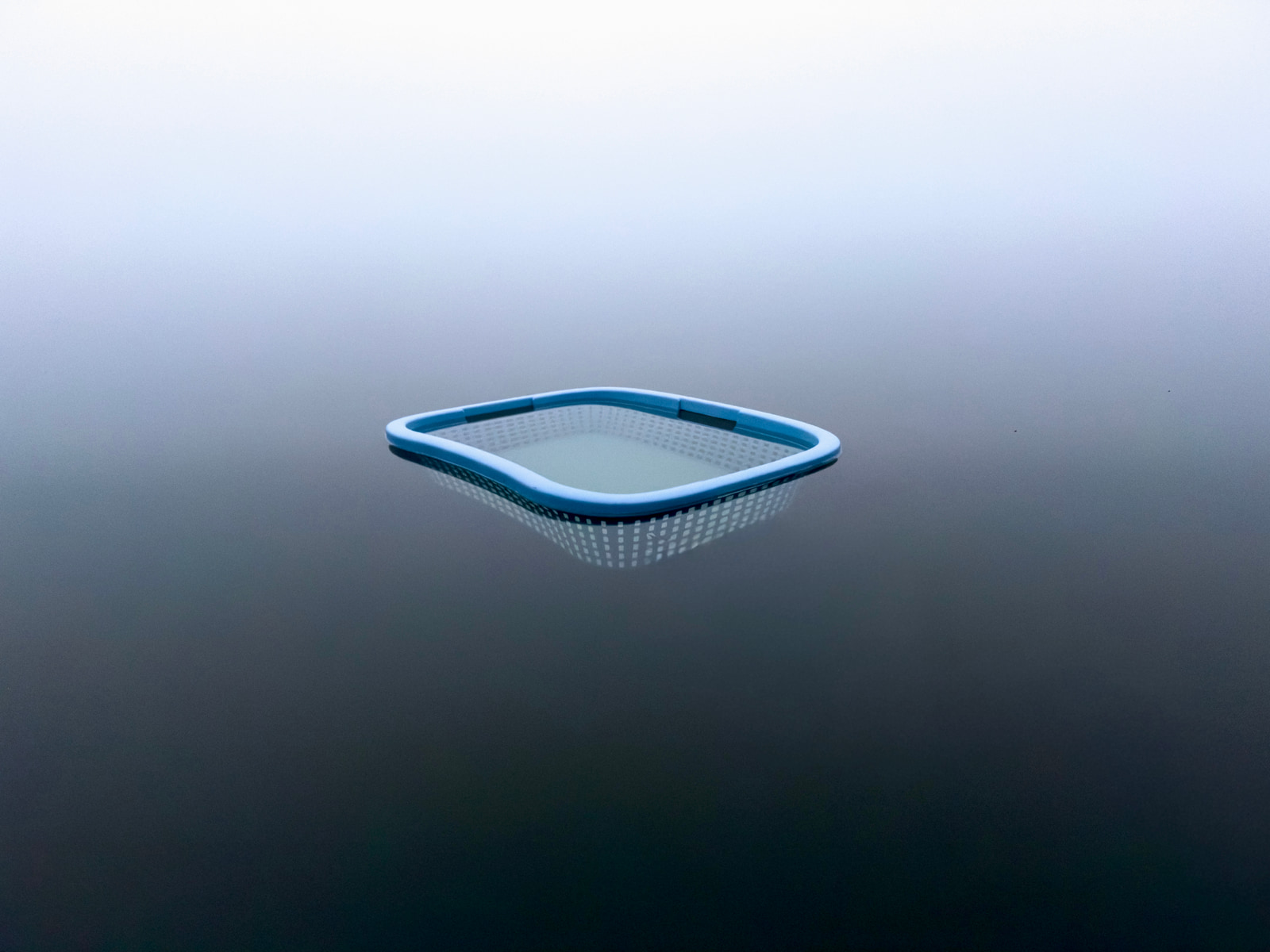 A light blue mesh strainer with a perforated surface floats against a plain gray background.