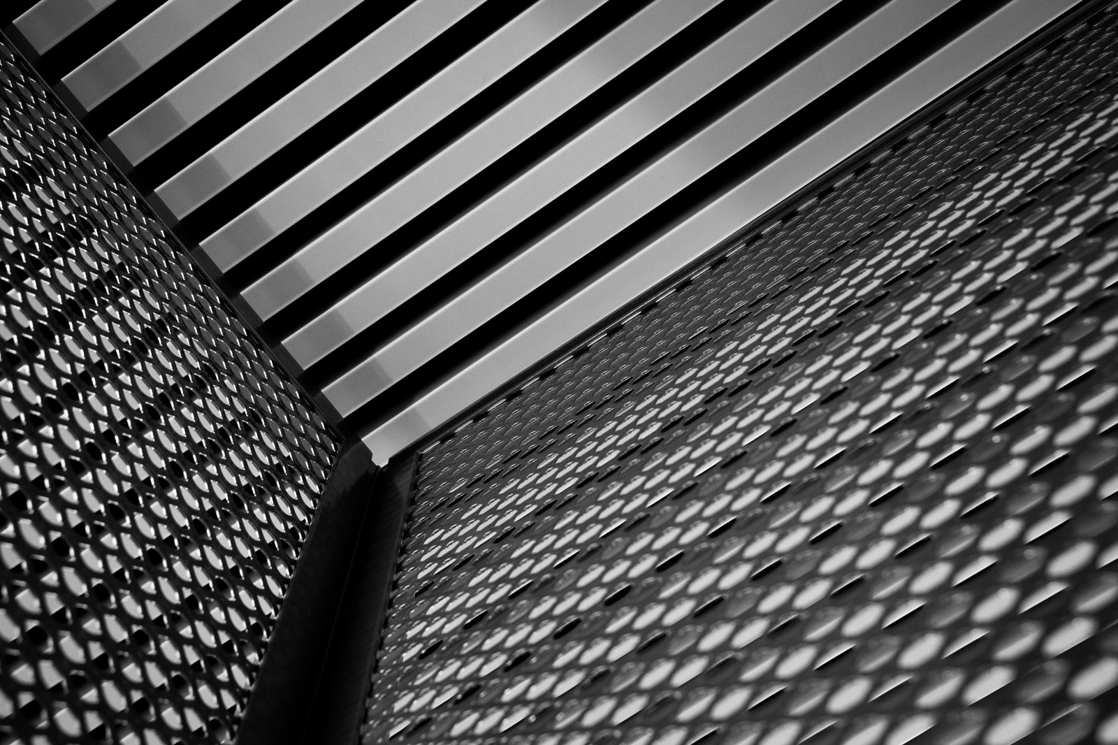 A close-up view of a textured metal surface with a perforated pattern, showing intersecting horizontal and diagonal lines.