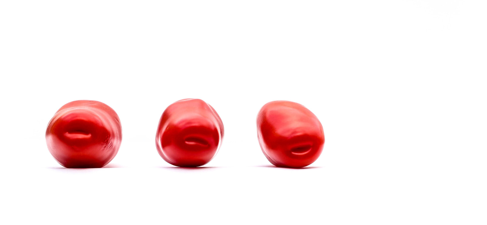 Three glossy red tomatoes arranged in a row on a white background.