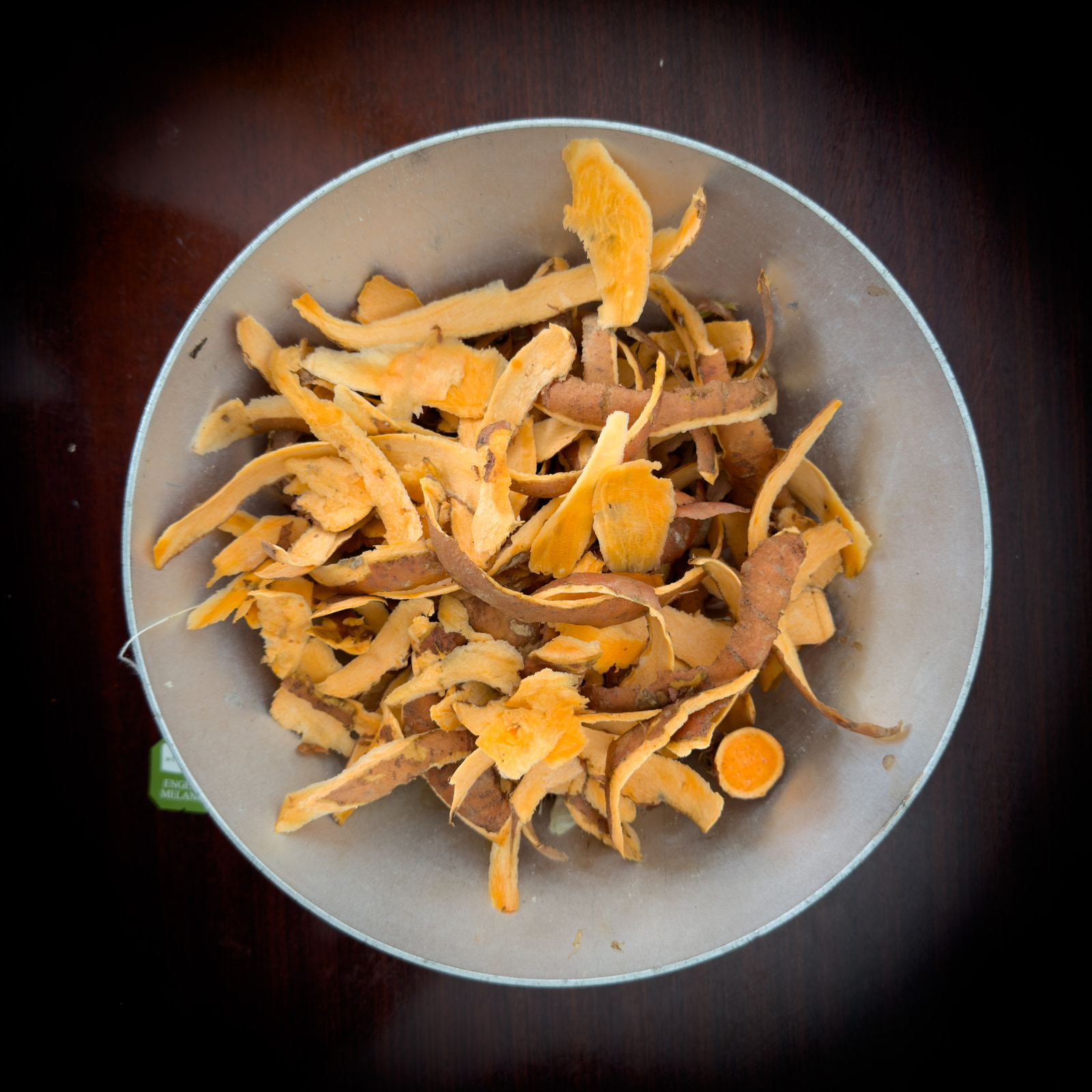 Shredded orange peel in a metal bowl on a dark wooden surface.