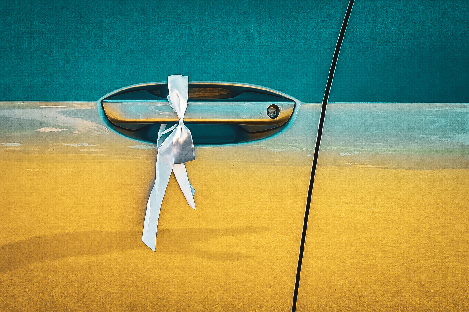 A silver ribbon is tied to the door handle of a yellow car.